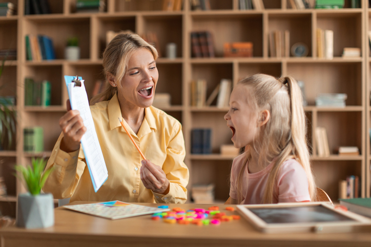 Cheerful female speech therapist curing child’s problems and impediments, little girl learning letters during lesson